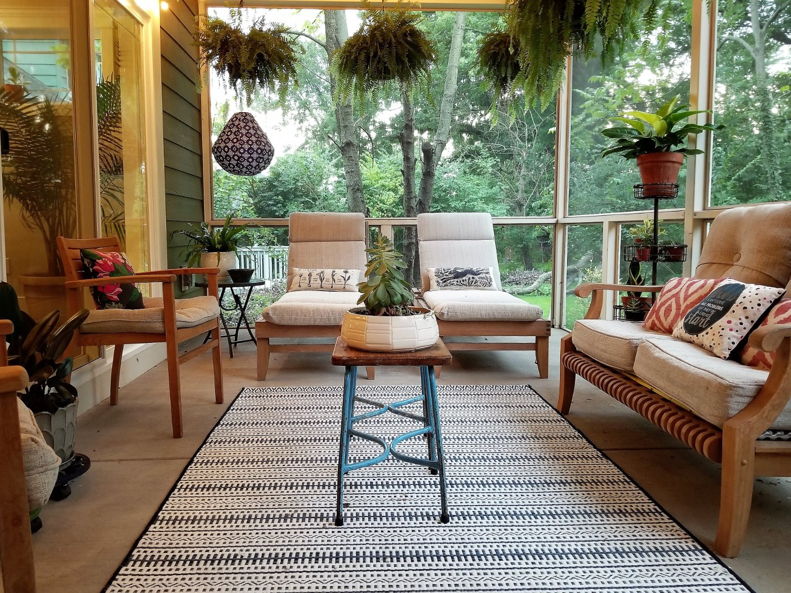 Maple Ave. screened porch seating area with a striped rug and hanging plants
